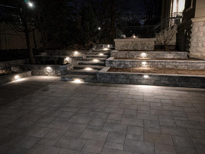 Backyard interlock patio lit at dusk with landscape lighting and steps