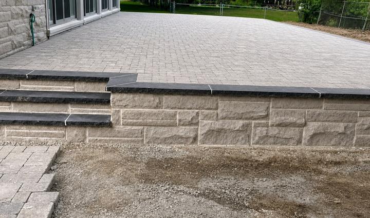 Engineered-block retaining wall under construction, holding back the grade beneath a paver surface