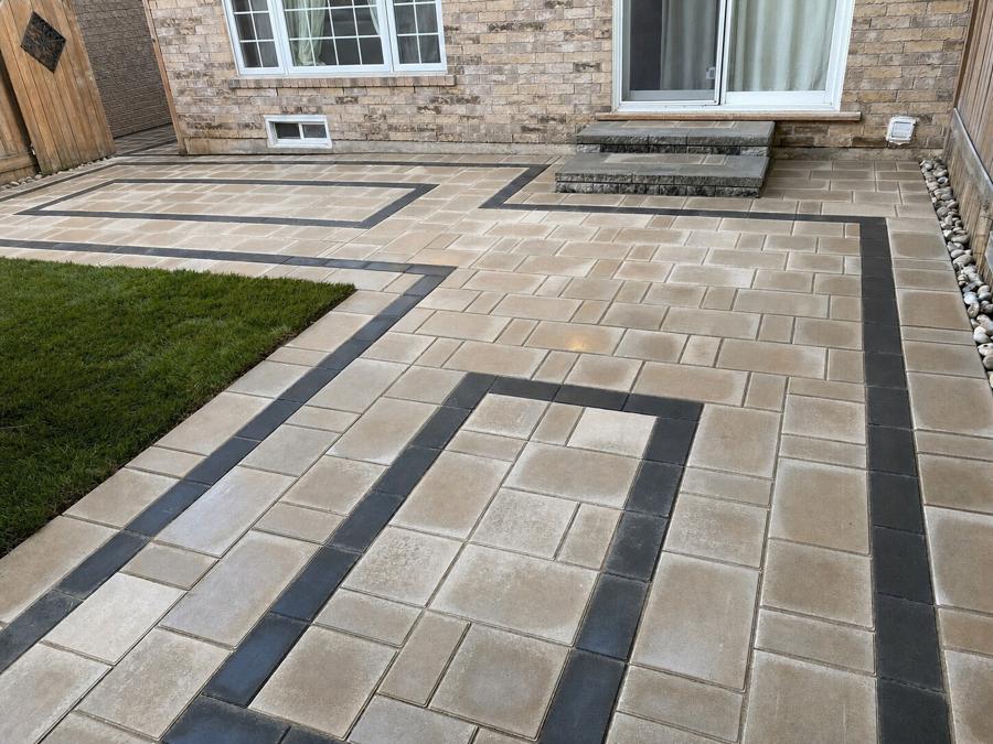 Backyard patio in beige slabs with an inlaid charcoal ribbon border