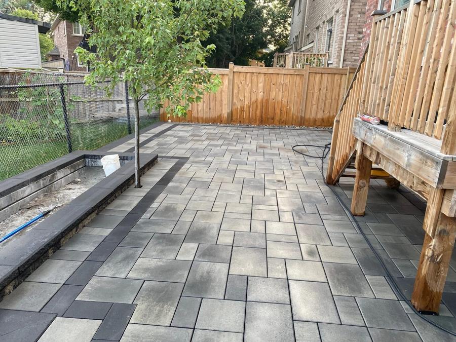 Grey paver patio with a raised tree planter beside wood steps