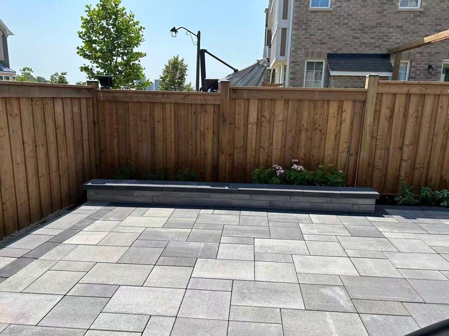Grey slab patio with a low seat wall and planting bed along a cedar fence
