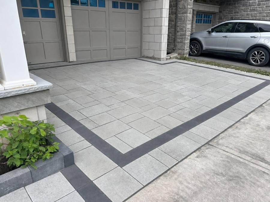 Grey paver driveway apron with a charcoal banded border in front of a double garage