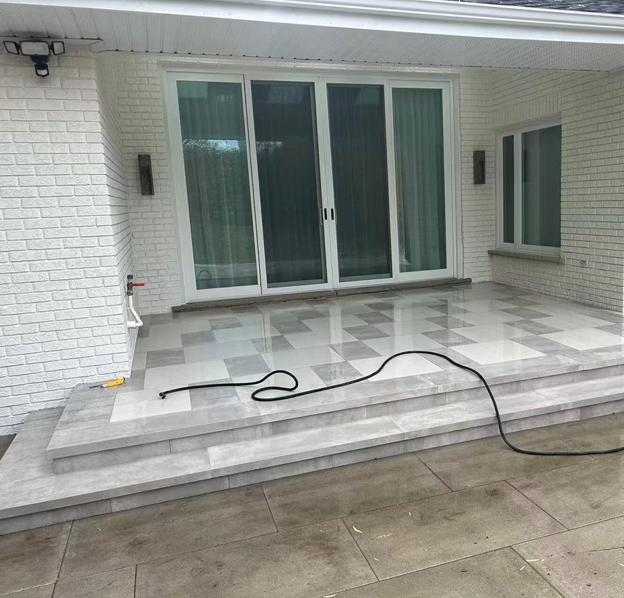 Raised patio in a light chequered stone laid against a white brick house, with a broad step down to the lower level