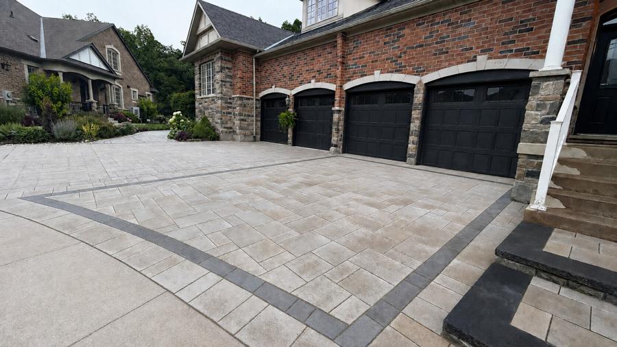 Wide interlock driveway with a curved charcoal border in front of a brick home and garages