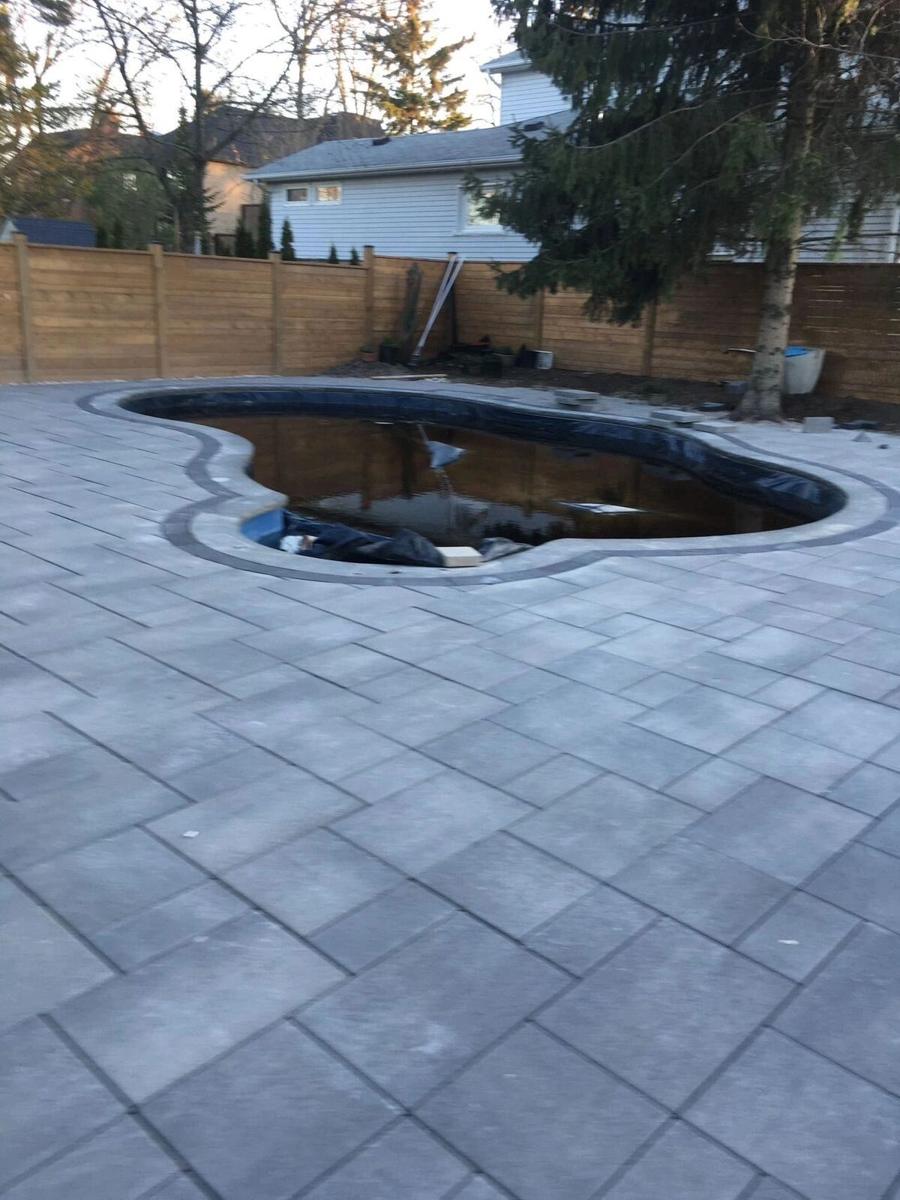 Grey paver surround with a dark border around an unfinished curved pool