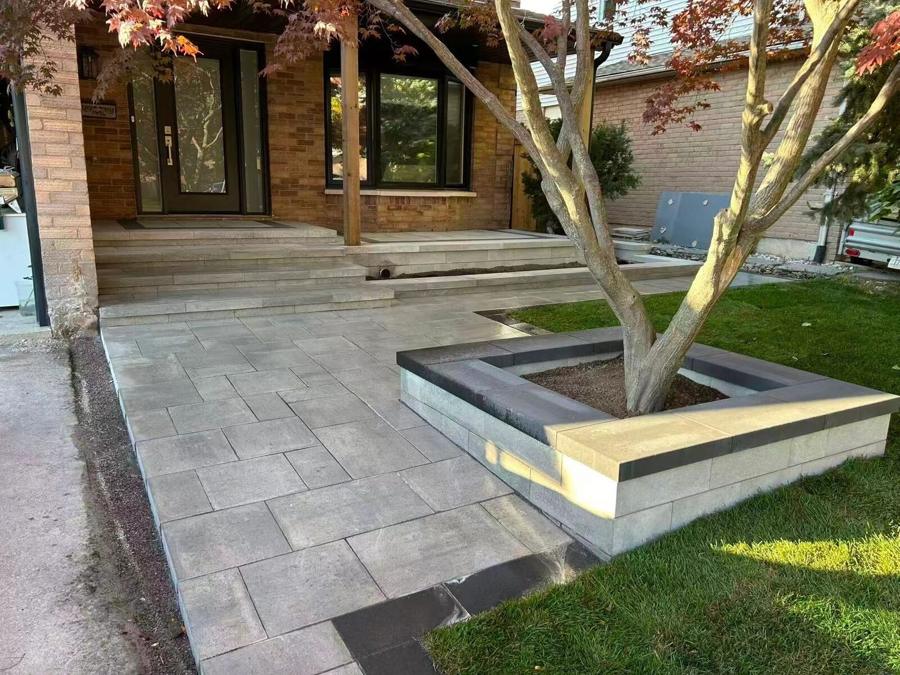 Raised block planter with pale coping around a tree beside a paver walkway and lawn