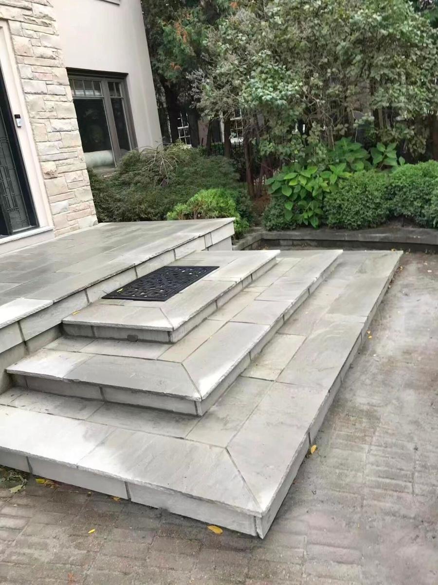 Broad pale stone entrance steps with angled corners beside shrubs