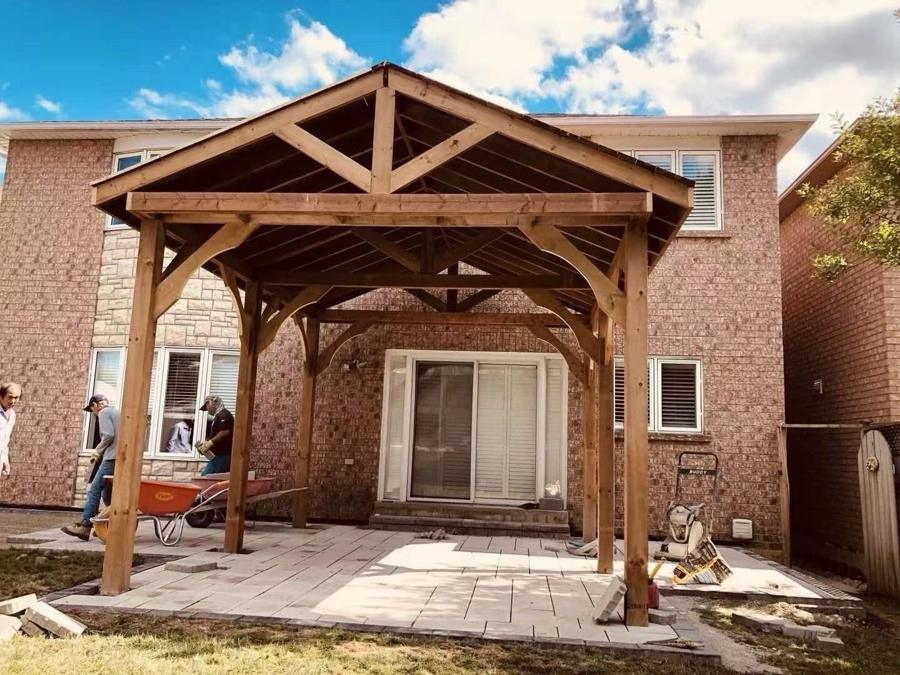 Timber pavilion with a pitched roof over a patio beside a brick home