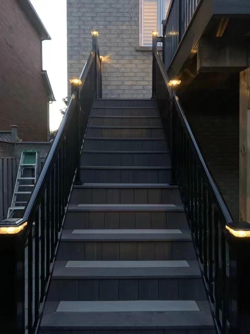Grey exterior staircase with black railings and illuminated post caps at dusk