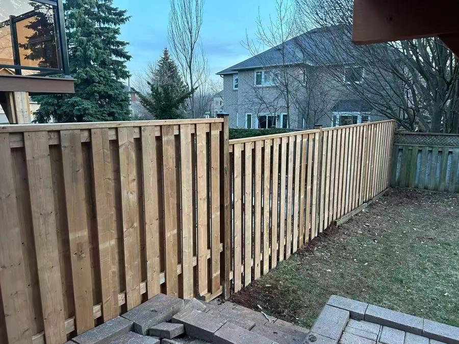 Vertical-board wood privacy fence beside a backyard lawn and paved steps