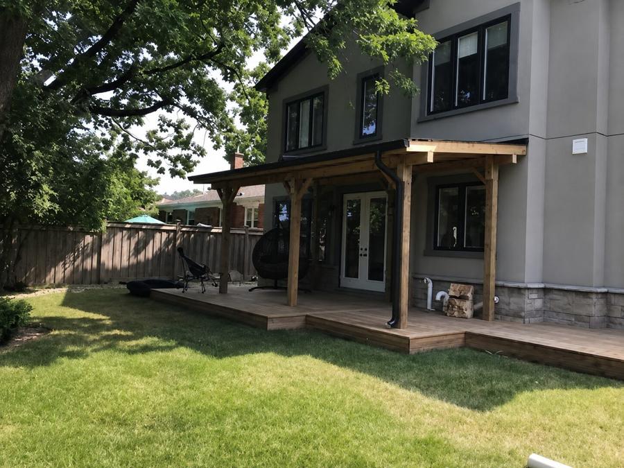 Covered deck with cedar posts running along the back of a house, opening onto a wide lawn