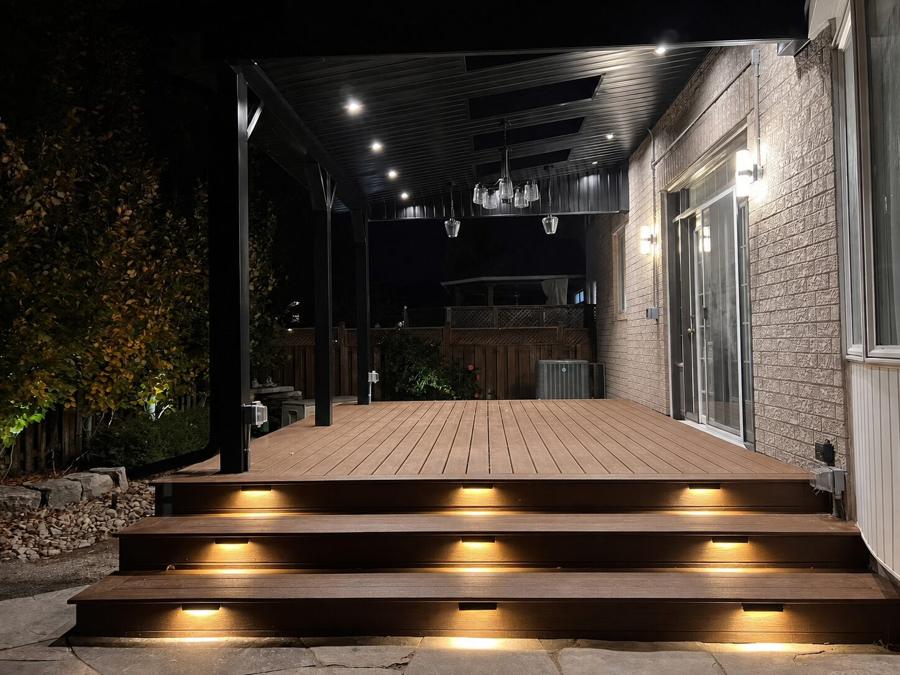 Covered deck at night with lit stair risers, pot lights and a hanging chandelier